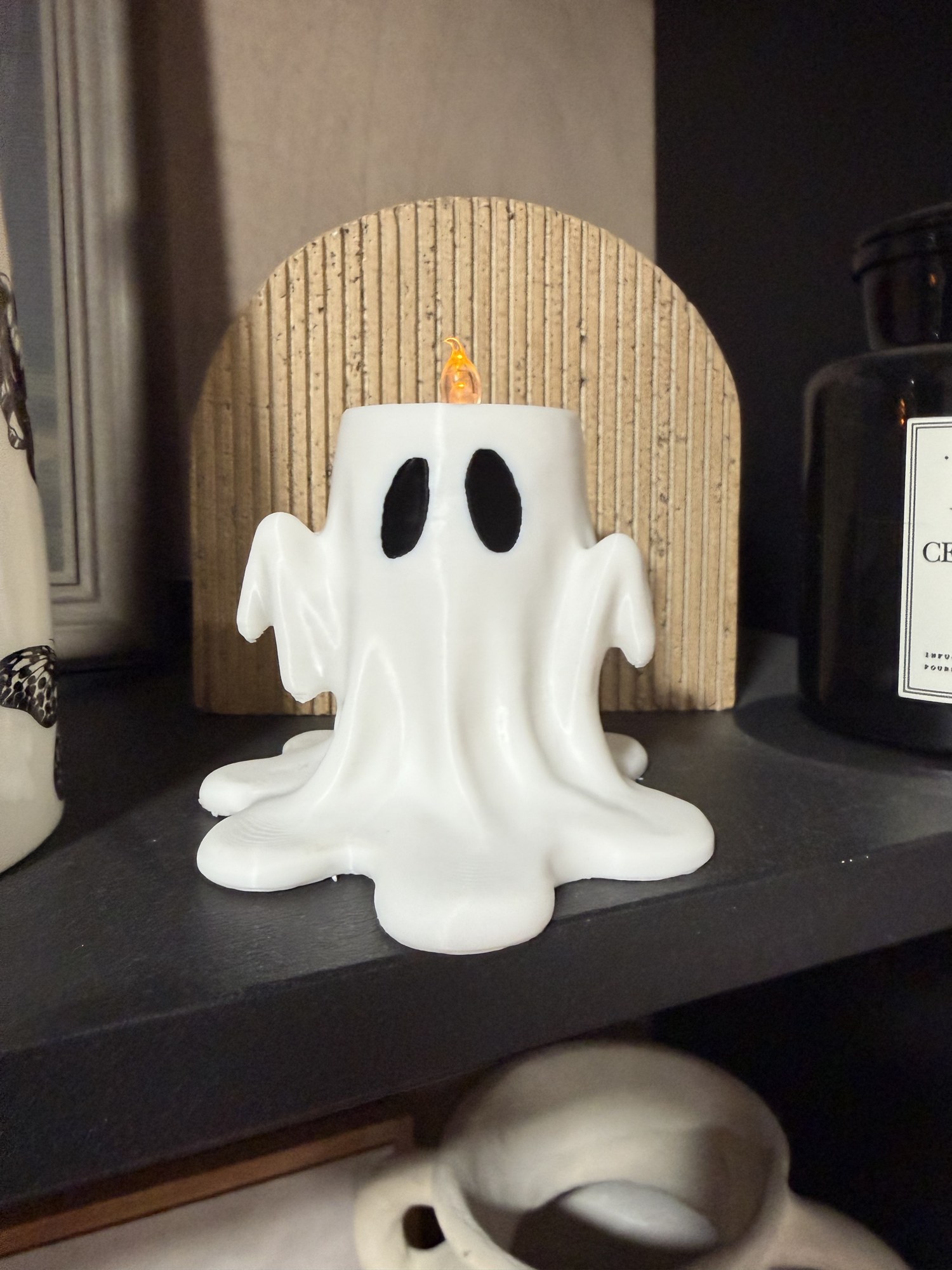 White Drippy Ghost tea light holder on a shelf against a wooden backdrop